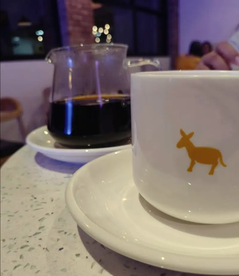 Café de filtrado en jarra de vidrio junto a una taza blanca con el burro mostaza de Zoco Brema