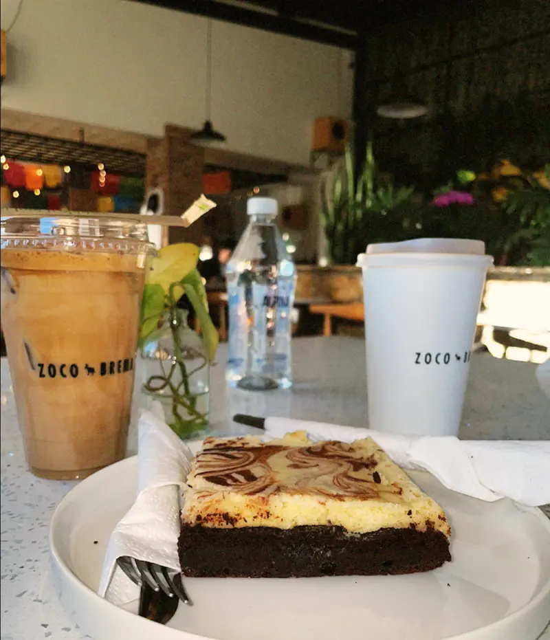 Terraza con plantas y mesa de terrazo, con un postre y bebidas de Zoco Brema
